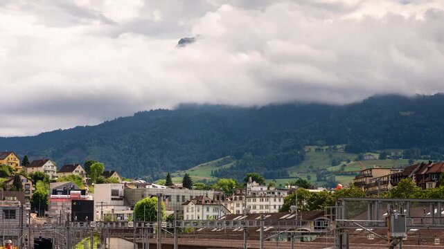 Lucerne railway station timelapse with rushing clouds engulfing Mount Pilatus peak, train yard and alpine foothills, Switzerland