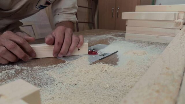 Extreme close up documentary footage of anonymous carpenter hands precisely pushing small raw wooden block over spinning router bit to shape edge on messy workbench inside local rustic joinery studio