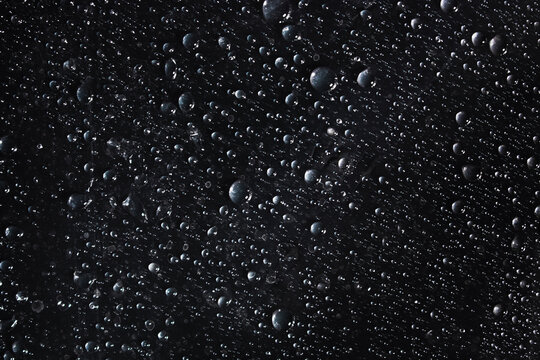 Real water droplets scattered across a black surface, photographed in close-up to create a detailed wet texture background.
