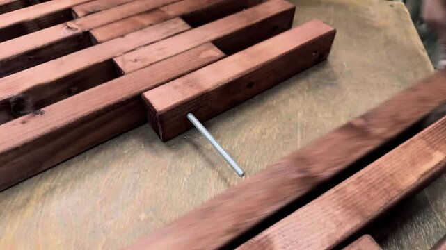 Extreme close up of unrecognizable male hands threading dark stained wooden timber blocks onto a metal bolt during a custom furniture assembly process inside a private enterprise domestic workshop