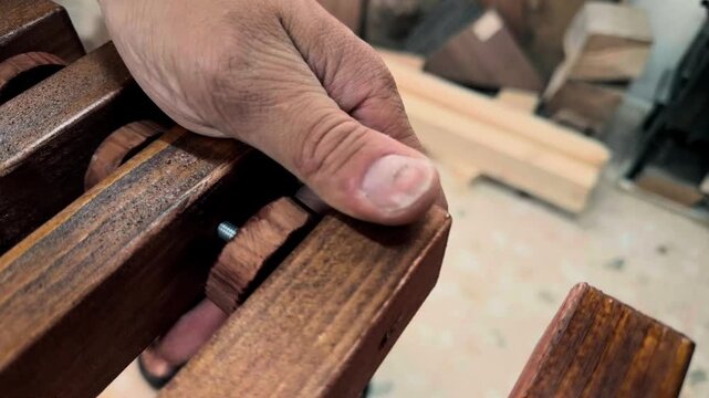 Handheld macro shot of an unrecognizable self employed tradesman pushing a small round wooden spacer onto a steel threaded rod during DIY furniture assembly in a private small scale crafting studio
