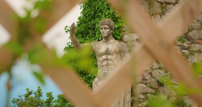 An ancient stone statue of Emperor Augustus stands behind wooden lattice on Monte Solaro in Capri Italy