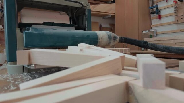 Professional carpenter feeding raw pine wood planks into thickness planer machine for surfacing timber blanks on wooden workbench during detailed manual labor process in authentic carpentry workshop