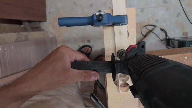 Unique tool mounted Snorricam point of view of anonymous joiner hands pressing heavy power drill into clamped plywood panel inside dusty workshop with rapidly rotating spinning background blur