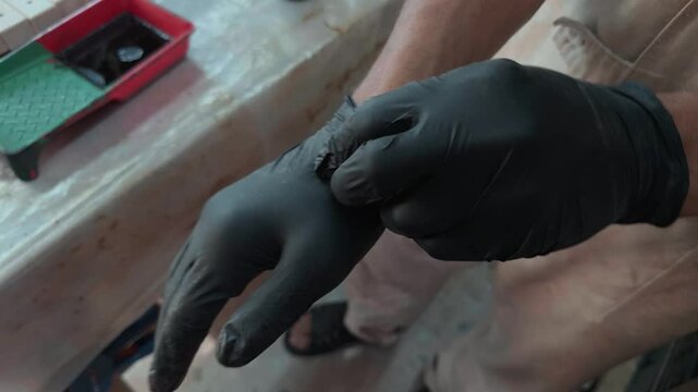 Unrecognizable professional carpenter putting on black rubber gloves and clapping hands together getting ready for wood staining process in authentic local manufacturing workshop close up shot