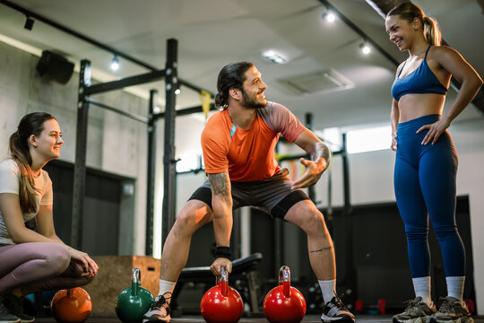 A personal trainer picking up a dumbbell to explain the correct posture to two women in a gym