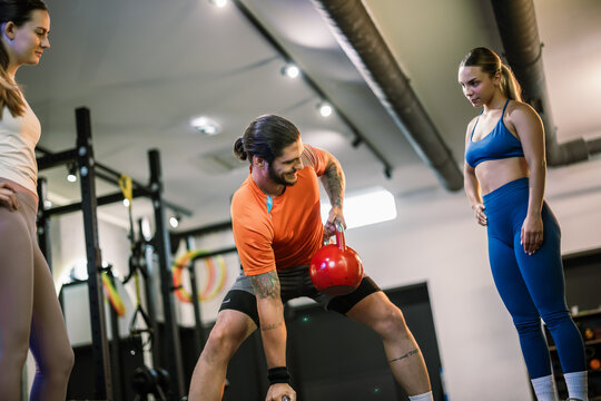 A personal trainer performing a dumbbell row exercise to show the correct form to two women