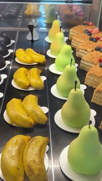 desserts in the form of a pear, banana in a showcase, cakes, also desserts in the form of currants, blueberries and coffee beans, also in the form of strawberries, such expensive desserts.