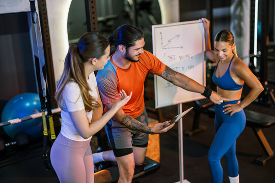 A personal trainer holding a tablet and pointing at a woman stomach to explain a core exercise in the gym.