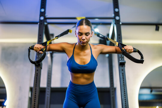Athletic young woman doing an intense chest press workout with suspension straps at the gym.