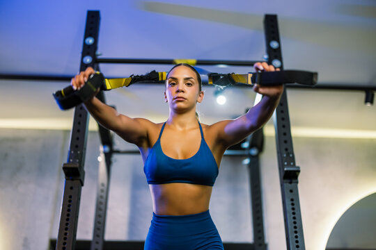 Focused young sportswoman exercising with suspension straps inside a modern fitness facility.