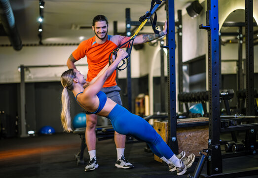 A personal trainer instructing a woman during a suspension strap inverted row exercise in a gym