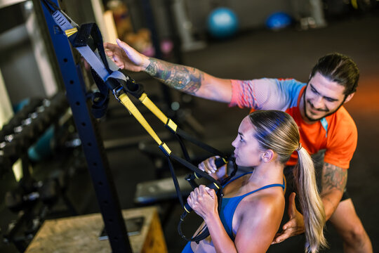 Fitness trainer assisting a young woman with her posture during a suspension strap workout
