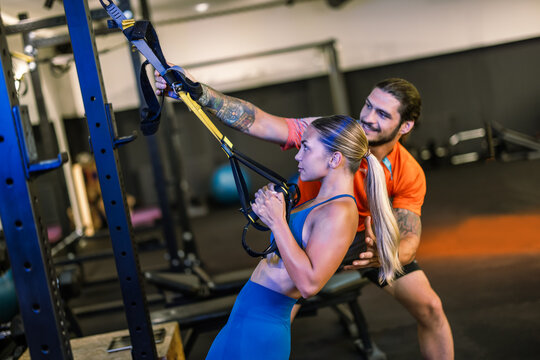 Standing fitness coach supervising a woman performing a suspension training row workout