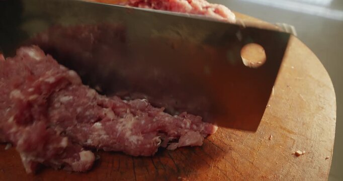 Pork mincing on a wooden chopping block with a cleaver
