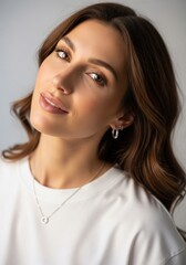 Fototapeta premium Close-up portrait of a cheerful young woman tilting her head playfully, wearing a casual white t-shirt, a silver chain necklace