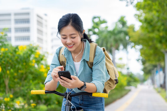 Smiling Asian businesswoman with a backpack, taking photos with her smartphone while standing on a city street on her way to work by bicycle.