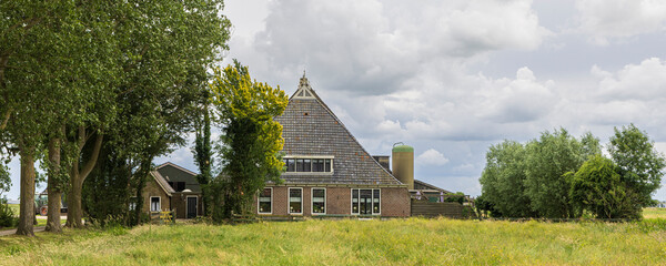 Obraz premium Traditional Dutch farmhouse in Friesland countryside with meadow, trees and overcast summer sky