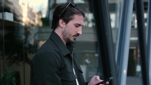 Confident man smiling while checking his mobile phone in front of a modern building