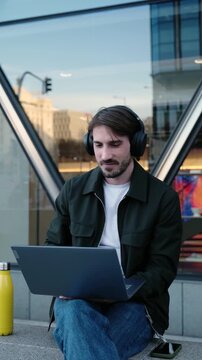 Digital nomad having a video call on a computer while sitting on stairs in a modern city street