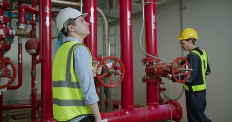 Two engineers conduct a detailed inspection of an industrial fire suppression system in a plant room, ensuring operational readiness and safety compliance. © HarryKiiM Stock