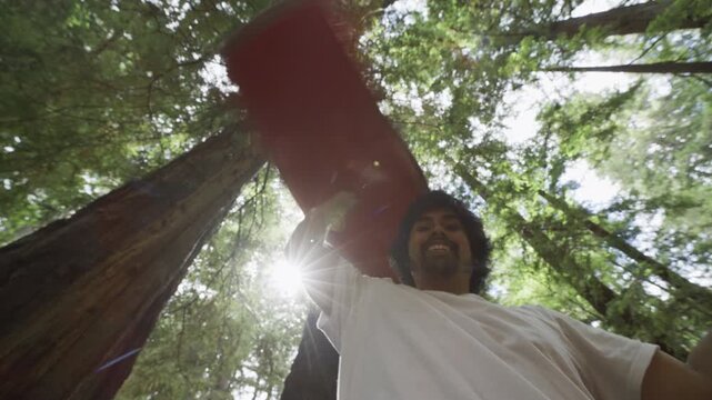 Man Raising Red Painted Board Overhead in Redwood Forest Low Angle