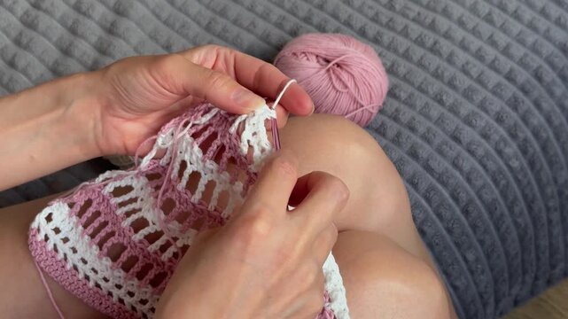 Young woman crocheting a stylish white and pink mesh sweater. The process of creating creative handmade clothing.