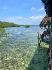 Fototapeta premium A tropical thatched hut on wooden stilts above clear turquoise water in Bocas del Toro, Panama. Bright midday sky