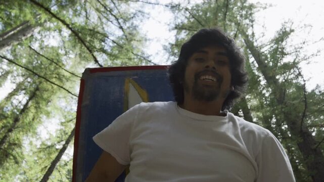 Happy Man Holding Blue Cross Board Overhead Among Trees Low Angle In Slow Motion