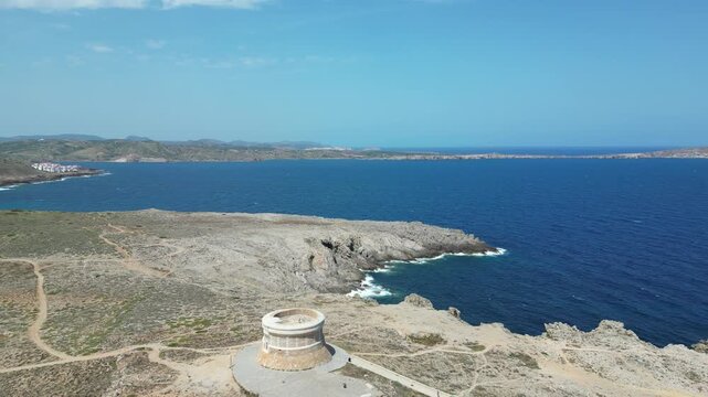 Aerial view of the historic Torre de Fornells watchtower situated on the rugged coastline overlooking the Mediterranean Sea in Fornells, Balearic Islands, Spain.