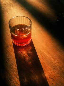 Single Glass of Amber Beverage with Ice on Wooden Counter - Dramatic Low Key Lighting and Hard Shadow Contrast