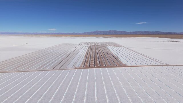 Drone aerial video of wide salt evaporation area and service tracks in Salinas Grandes, Argentina under clear sky.