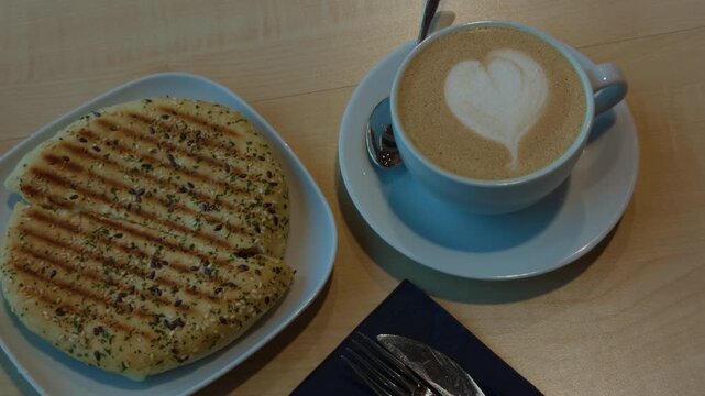 Latte art coffee cup beside grilled flatbread on plates with utensils at cozy cafe table