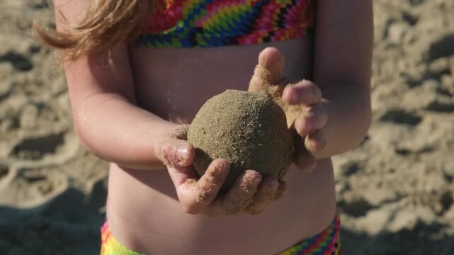 Close up of child hands holding wet round sand ball on beach. Concept of creative kid summer games