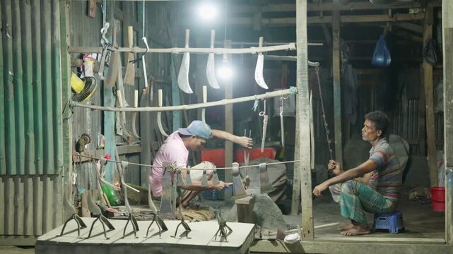 Traditional South Asian Bangladeshi blacksmith reshaping glowing red-hot metal sickles with hammer on anvil