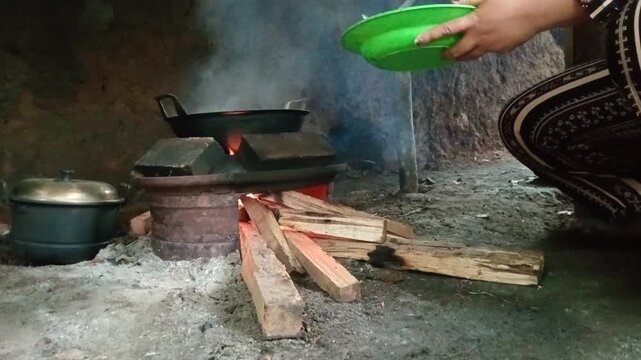 Village woman cooking fresh fish over a traditional wood burning stove in a rustic kitchen
