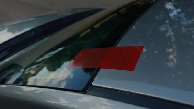 Red tape marking on car windshield and roof seam with reflections on glossy metallic surface