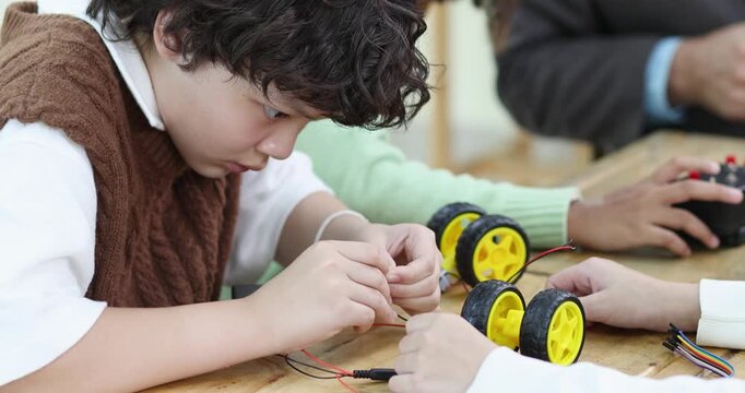 Elementary students assembling a robot car and connecting electronic wires in a STEM classroom. Hands-on learning, robotics, engineering, teamwork and back to school concept