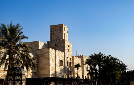 Horizontal wide shot of traditional sand-colored Arabic stone architecture featuring wind towers and crenellated parapets,Souk Madinat Jumeirah, Duba