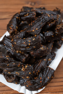 Dried beef strips sprinkled with sesame seeds are piled on a white paper plate at vertical composition