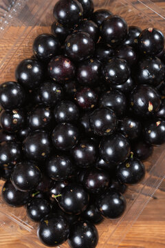 Plump jabuticaba berries are packed inside a clear plastic fruit container on a wooden table