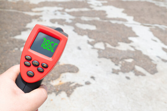 a red digital infrared thermometer measuring the temperature of outdoor cracked concrete pavement