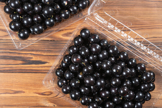 Plump jabuticaba berries are packed inside a clear plastic fruit container on a wooden table