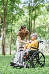 Fototapeta premium Young caregiver supporting an elderly woman in a wheelchair during a park walk outdoors