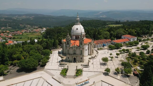 Aerial view of the Sanctuary of Our Lady of Sameiro with its iconic white dome and red tiled roof set in a large paved plaza surrounded by lush trees in Braga, Braga, Portugal.
