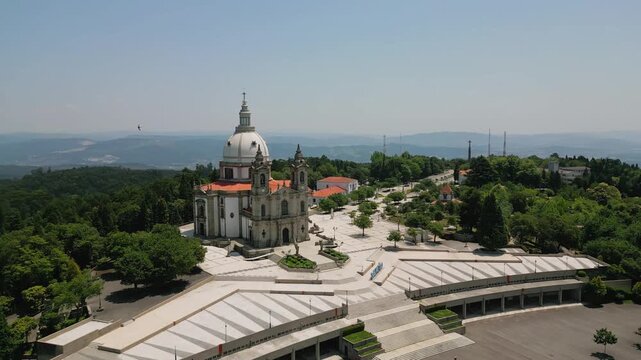 Aerial view of the Sanctuary of Our Lady of Sameiro with its grand dome, neoclassical architecture, and expansive paved plaza surrounded by lush green hills in Braga, Braga, Portugal.