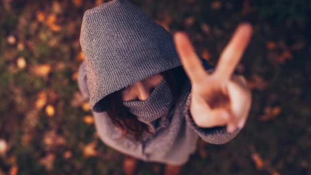 A person wearing a hoodie and making the peace sign with their hand.