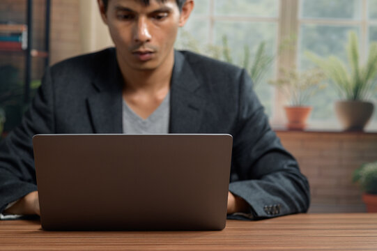 Businessman Working on Laptop in Modern Office with Natural Light and Indoor Plants
