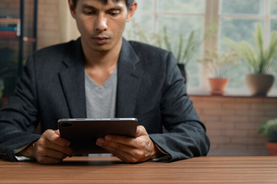 Professional young man using tablet at desk in modern indoor space with plants