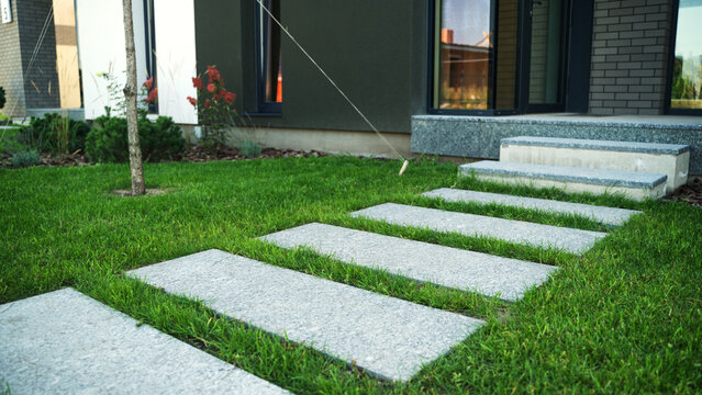 Granite stepping stones form a path across vibrant green grass, leading to a modern home that blends architecture with nature